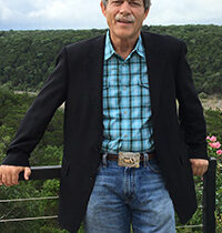jake hersman an agent at texas ranch brokers standing on a fence overlooking a ranch in burnet county texas