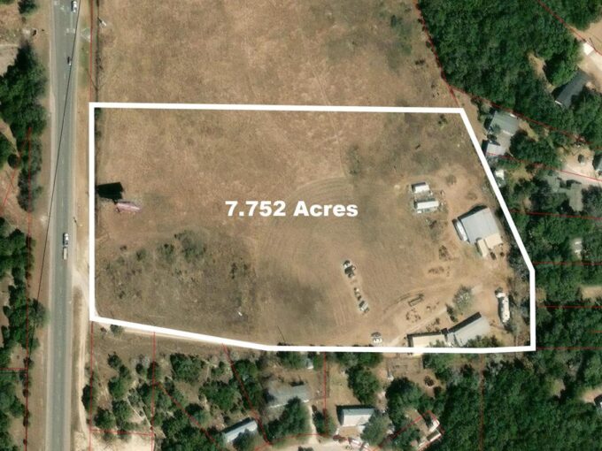 Aerial view of a fenced plot of land labeled 7.752 Acres, showing a mostly open field with a few scattered buildings and trees around the perimeter. A road runs along the left side of the plot.